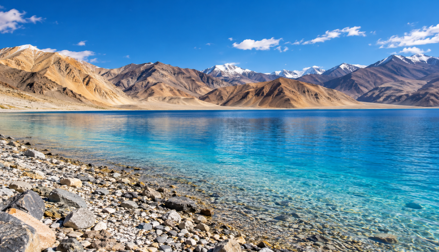 Illustration inspired by Pangong Lake in Ladakh, with turquoise water, a rocky shoreline and barren mountains.